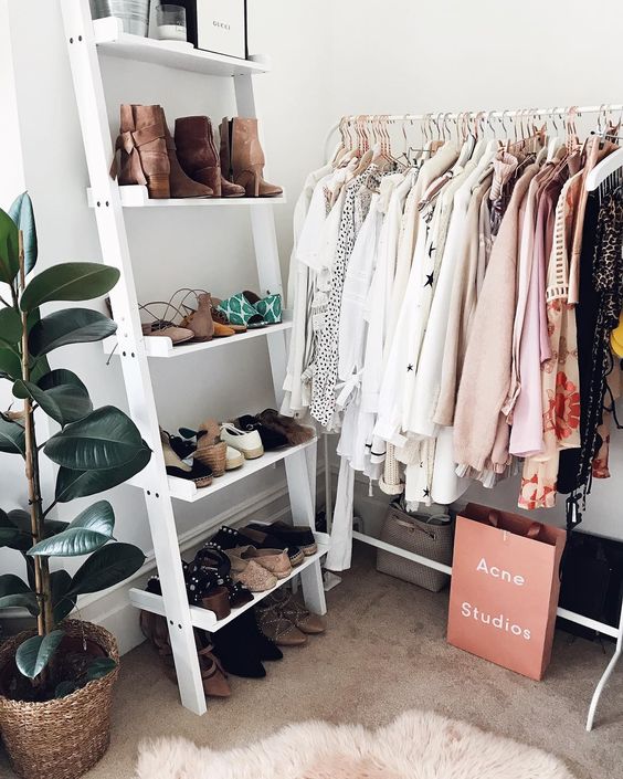 makeshift closet corner with clothing rack and ladder shoe shelf.